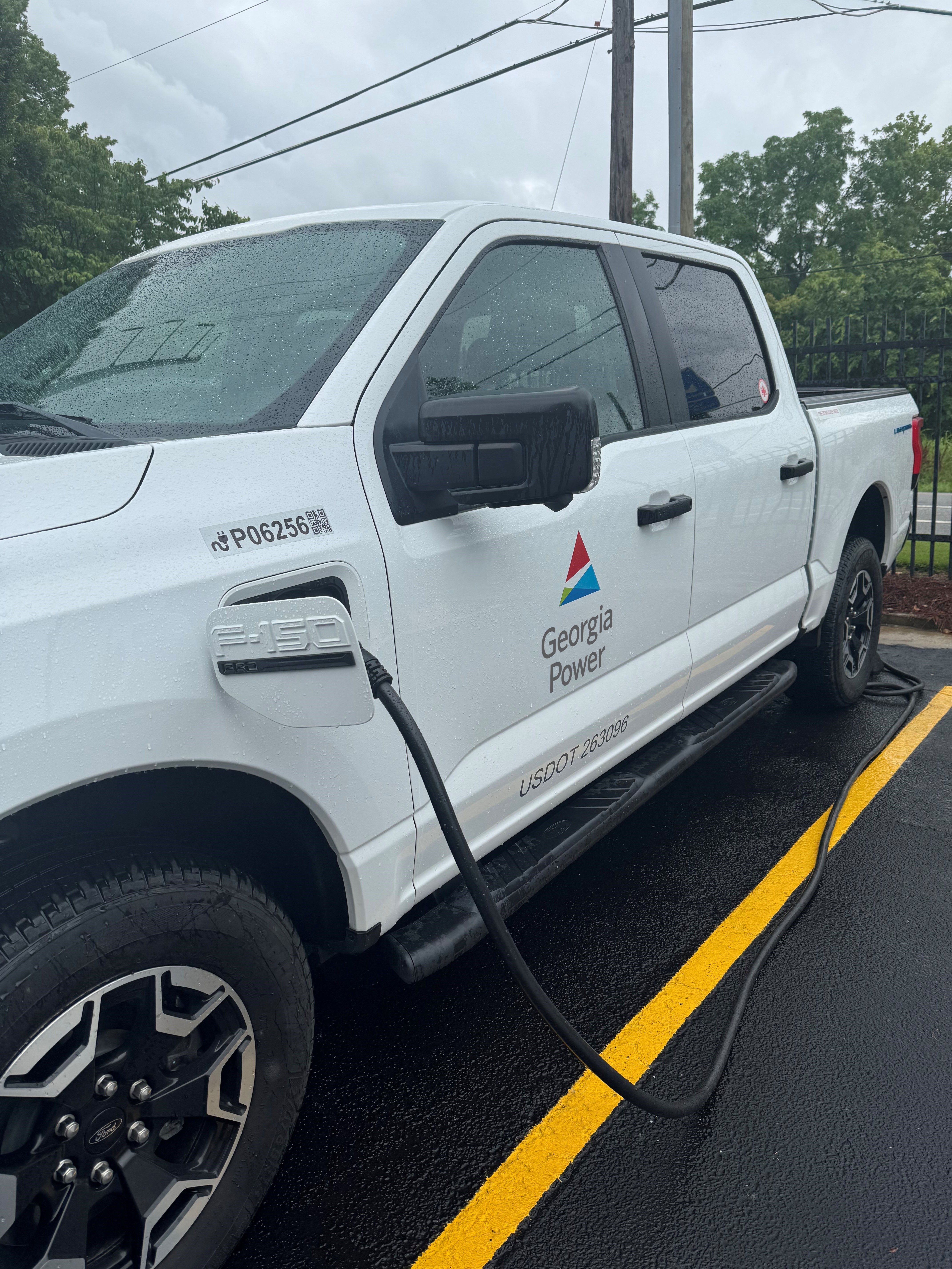 A white truck with "Georgia Power" on the door is plugged into a charger